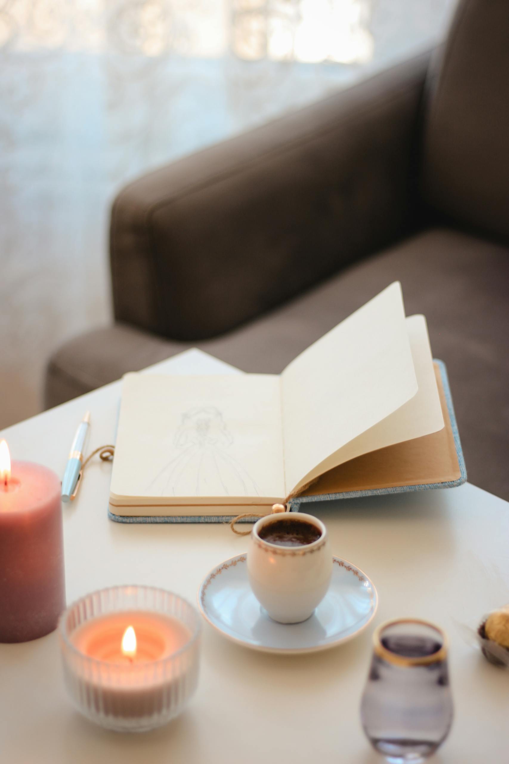 Relaxing indoor scene with coffee, candles, and an open notebook on a table.
